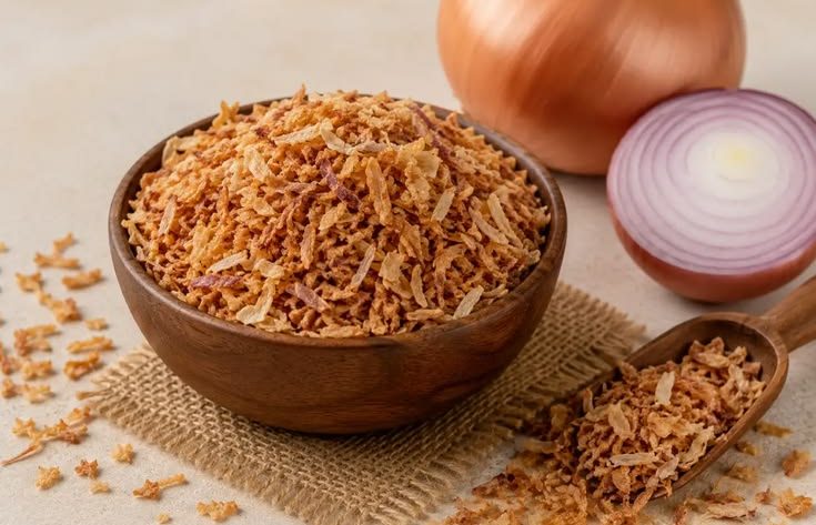 Prosesnya cukup sederhana, tetapi beberapa detail menentukan tekstur akhir. Bawang yang terlalu tebal sulit kering merata, sedangkan irisan terlalu tipis mudah berubah warna sebelum bagian dalamnya matang. Karena itu, siapkan alat, wadah peniris, dan tempat penyimpanan sebelum mulai menggoreng agar setiap tahap berjalan lancar. Cara Membuat Bawang Goreng Renyah 1. Pilih Bawang dengan Kondisi Baik Gunakan bawang merah yang masih segar, padat, tidak bertunas, dan bebas dari bagian busuk. Bawang dengan kadar air serta ukuran yang relatif seragam membantu irisan matang lebih merata saat digoreng. Kupas kulitnya, lalu buang bagian yang rusak sebelum mencuci bawang. Setelah mencuci, tiriskan dan keringkan permukaannya agar air tidak memicu percikan minyak ketika proses penggorengan dimulai. Langkah ini juga membantu minyak tetap stabil dan mengurangi risiko bawang saling menempel. 2. Iris dengan Ketebalan Seragam Iris bawang secara tipis dan konsisten supaya setiap potongan matang dalam waktu yang hampir sama. Pisau tajam dapat membantu pekerjaan skala kecil, sedangkan usaha dengan produksi lebih banyak bisa mempertimbangkan mesin perajang bawang dari Rumah Mesin agar proses pengirisan lebih cepat dan seragam. Jangan menumpuk irisan terlalu lama dalam keadaan basah karena kelembapan dapat membuat hasil gorengan kurang garing. Sebarkan irisan di atas wadah bersih dan biarkan permukaannya mengering sebelum masuk ke minyak. Jika menyiapkan banyak bawang, kerjakan secara bertahap agar irisan yang menunggu tidak menumpuk terlalu lama. 3. Gunakan Bumbu Secukupnya Sebagian orang menambahkan sedikit garam untuk memperkuat rasa bawang goreng. Jika memakai garam, campurkan tipis dan merata, lalu segera goreng agar bumbu tidak menarik terlalu banyak air dari irisan bawang. Pelaku usaha makanan juga bisa membuat satu uji coba tanpa tambahan bumbu untuk mengetahui rasa alami bawang. Hindari menambahkan banyak tepung jika ingin menghasilkan bawang goreng dengan tekstur ringan dan rasa bawang yang tetap menonjol. 4. Atur Suhu dan Jumlah Minyak Panaskan minyak dengan api sedang dan pastikan minyak cukup untuk membuat irisan terendam atau bergerak leluasa. Masukkan bawang dalam jumlah kecil agar suhu minyak tidak turun drastis dan irisan tidak saling menempel. Aduk perlahan selama menggoreng supaya panas menjangkau seluruh bagian. Saat bawang mulai berwarna kuning keemasan, segera angkat karena sisa panas masih dapat membuat warnanya semakin gelap setelah keluar dari penggorengan. Hindari meninggalkan wajan tanpa pengawasan karena perubahan warna dapat berlangsung cepat pada tahap akhir. 5. Tiriskan dan Dinginkan dengan Benar Angkat bawang sebelum warnanya menjadi cokelat tua, kemudian tiriskan menggunakan saringan atau kertas penyerap minyak khusus makanan. Sebarkan bawang di atas wadah lebar agar uap panas cepat keluar dan bagian bawahnya tidak menahan kelembapan. Jangan langsung memasukkan bawang yang masih panas ke dalam stoples. Tunggu sampai suhunya turun dan teksturnya kering, sebab uap yang terperangkap dapat membuat bawang cepat melempem. Pastikan wadah penyimpanan tidak menyimpan sisa air dari proses pencucian atau pemakaian sebelumnya. 6. Simpan dalam Wadah Kedap Udara Masukkan bawang goreng yang sudah dingin ke wadah kering dan kedap udara, lalu letakkan di tempat sejuk serta jauh dari sinar matahari. Gunakan sendok yang bersih dan kering setiap kali mengambilnya agar kelembapan tidak masuk ke dalam wadah. Untuk produksi rutin, buat catatan tanggal penggorengan dan jumlah hasil agar stok lama bisa digunakan lebih dulu. Informasi mengenai peralatan pengolahan pangan juga dapat ditemukan melalui situs Rumah Mesin sebagai referensi saat usaha membutuhkan proses kerja yang lebih efisien. Kesimpulan Cara membuat bawang goreng renyah bergantung pada kualitas bawang, ketebalan irisan, pengaturan suhu minyak, dan proses penirisan. Kerjakan setiap tahap dengan rapi agar bawang matang merata dan tidak menyerap minyak berlebihan. Setelah dingin, simpan hasil gorengan dalam wadah kedap udara untuk menjaga kerenyahannya. Jika membuat dalam jumlah besar, pertimbangkan alat perajang yang sesuai kapasitas supaya ukuran irisan lebih konsisten dan waktu persiapan lebih efisien.